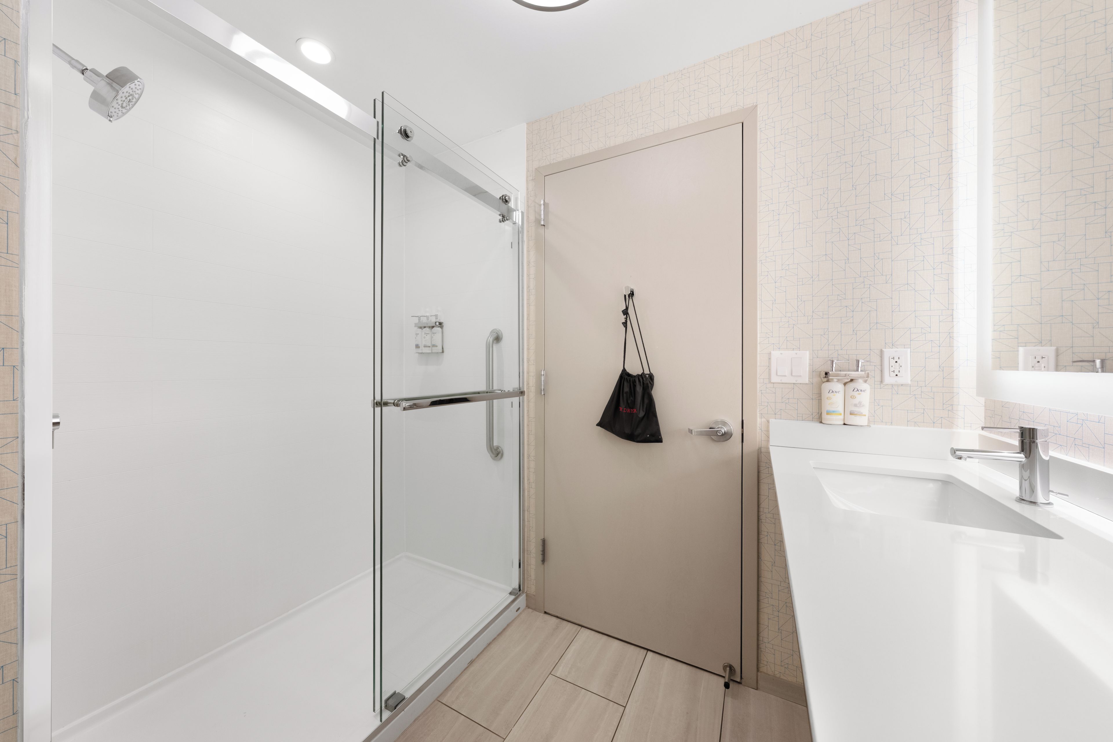A modern bathroom with a glass shower enclosure, a white sink, and a towel hanging on the door.