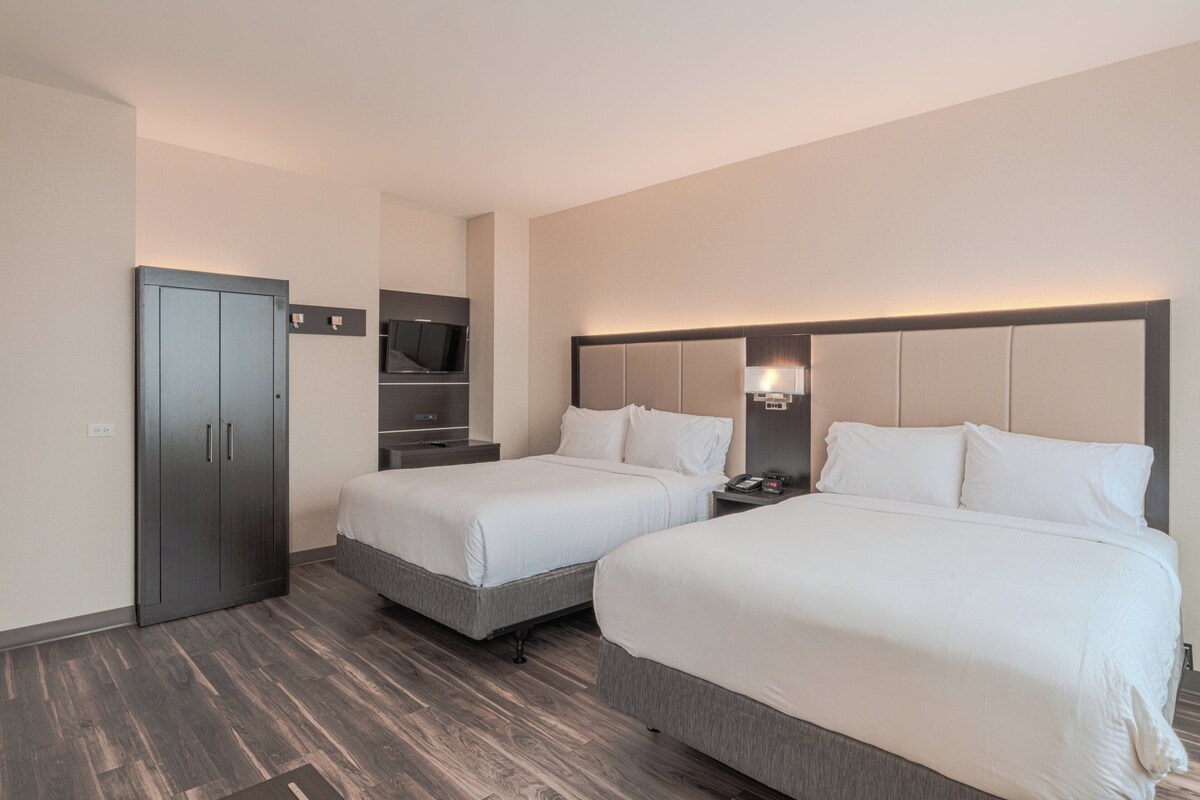 Una habitación de hotel con dos camas, un armario, un televisor y una mesita de noche.