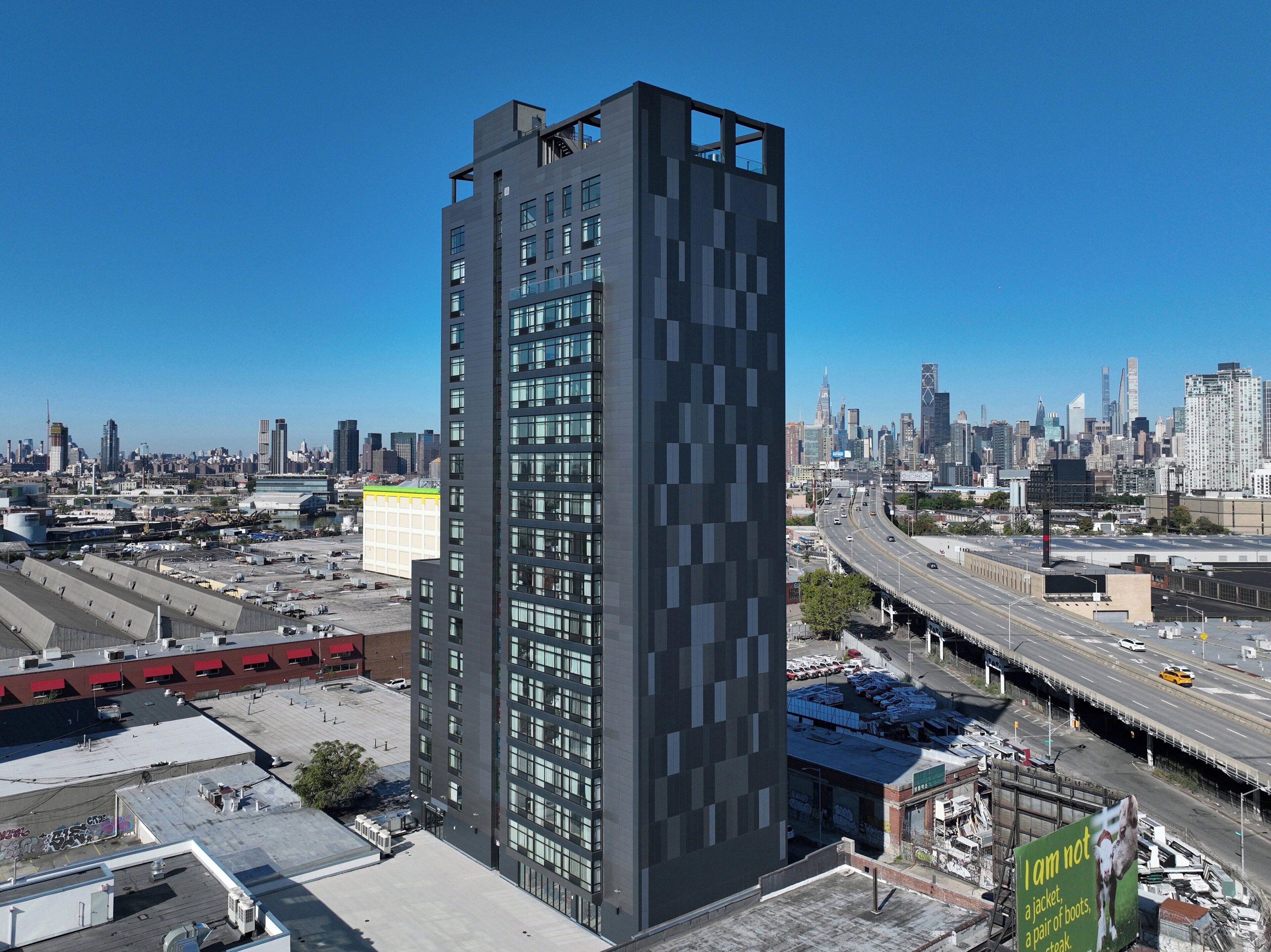 A modern high-rise building with a grid-like facade, surrounded by a busy urban environment with a highway and other buildings in the background.