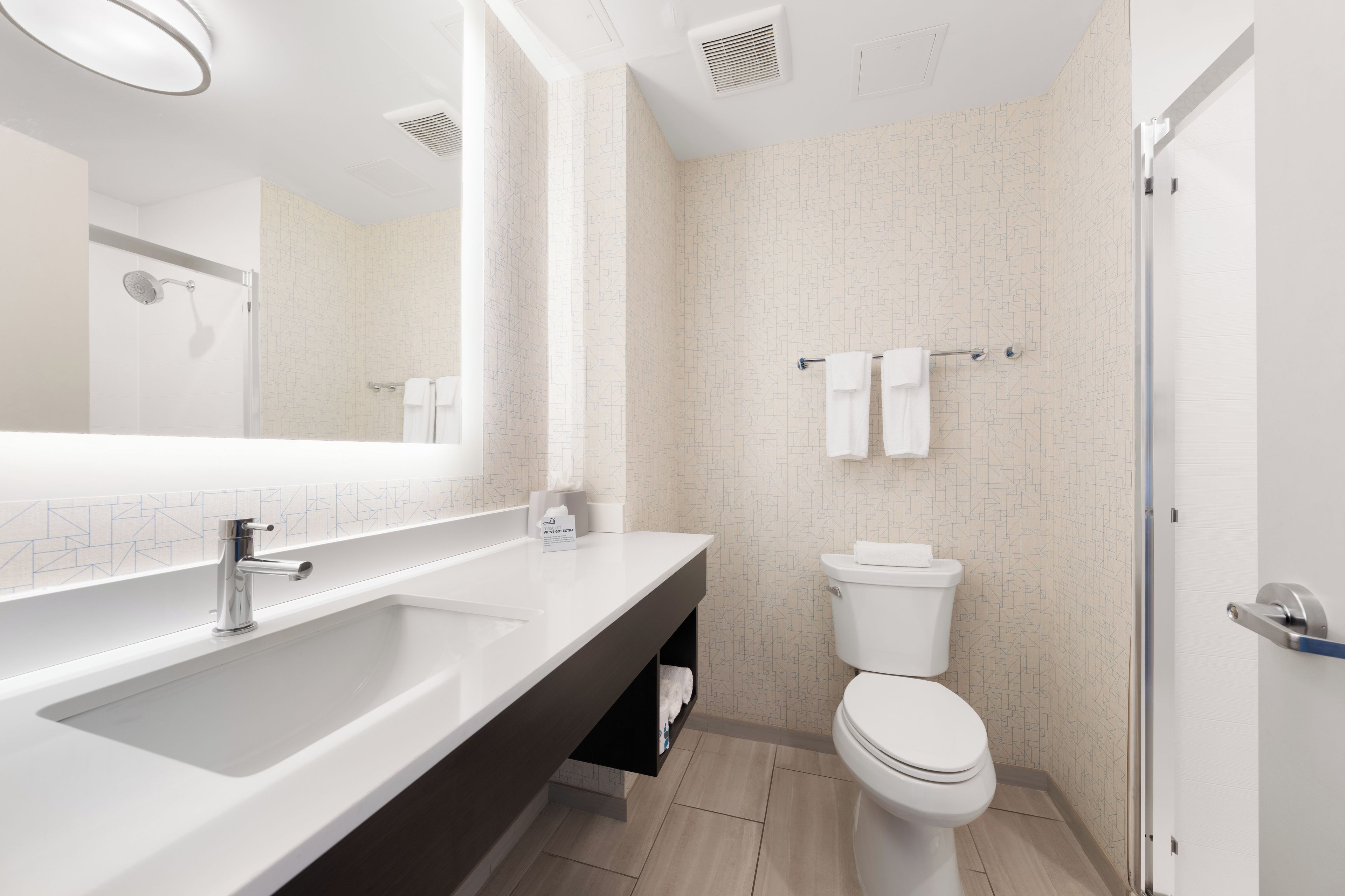 A modern bathroom with a large mirror, a sink, a toilet, and a shower.