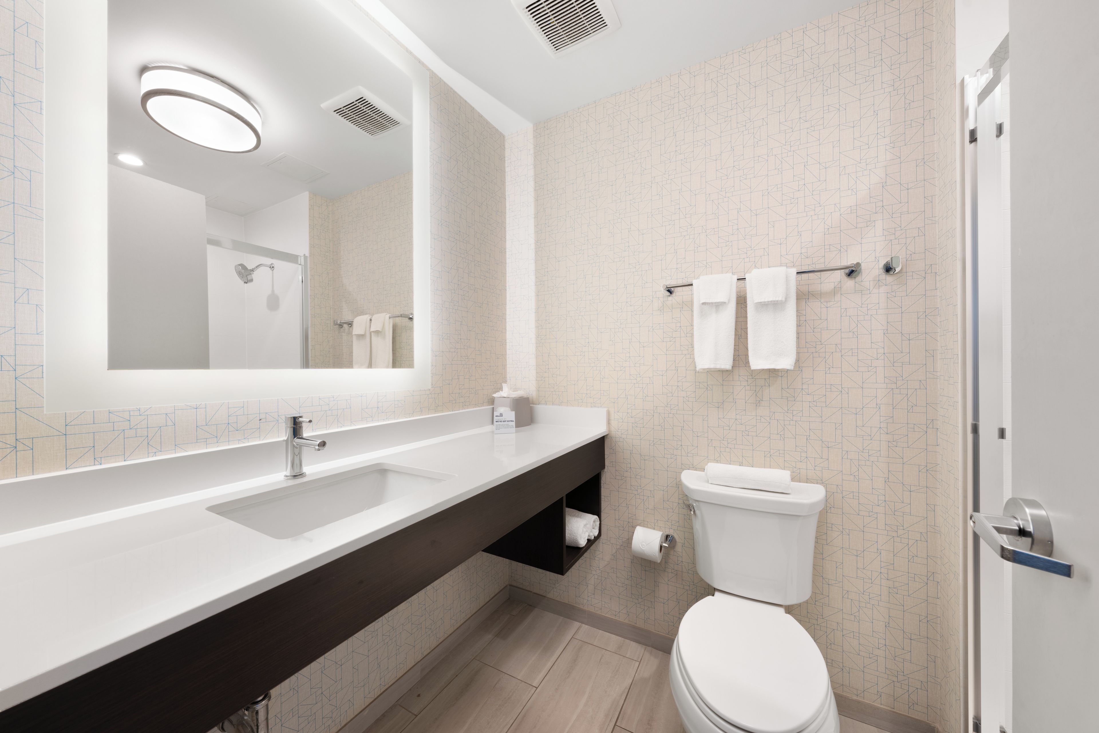 A modern bathroom with a large mirror, a sink, a toilet, and a shower area.
