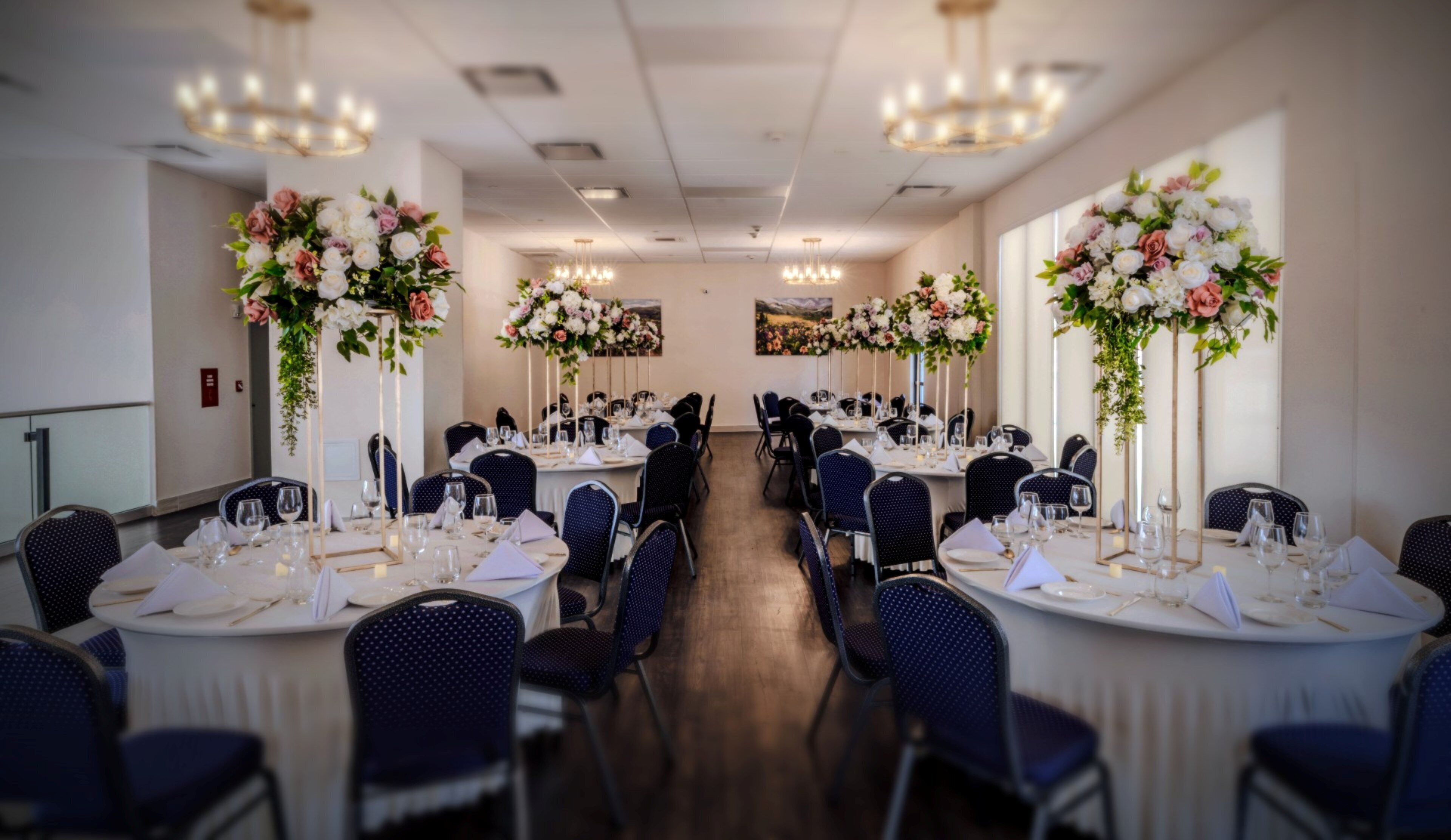 A banquet hall with round tables, blue chairs, and floral centerpieces.