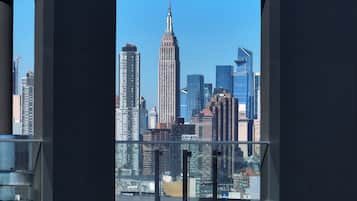A cityscape with the Empire State Building prominently in the center, viewed through a window with a dark frame.