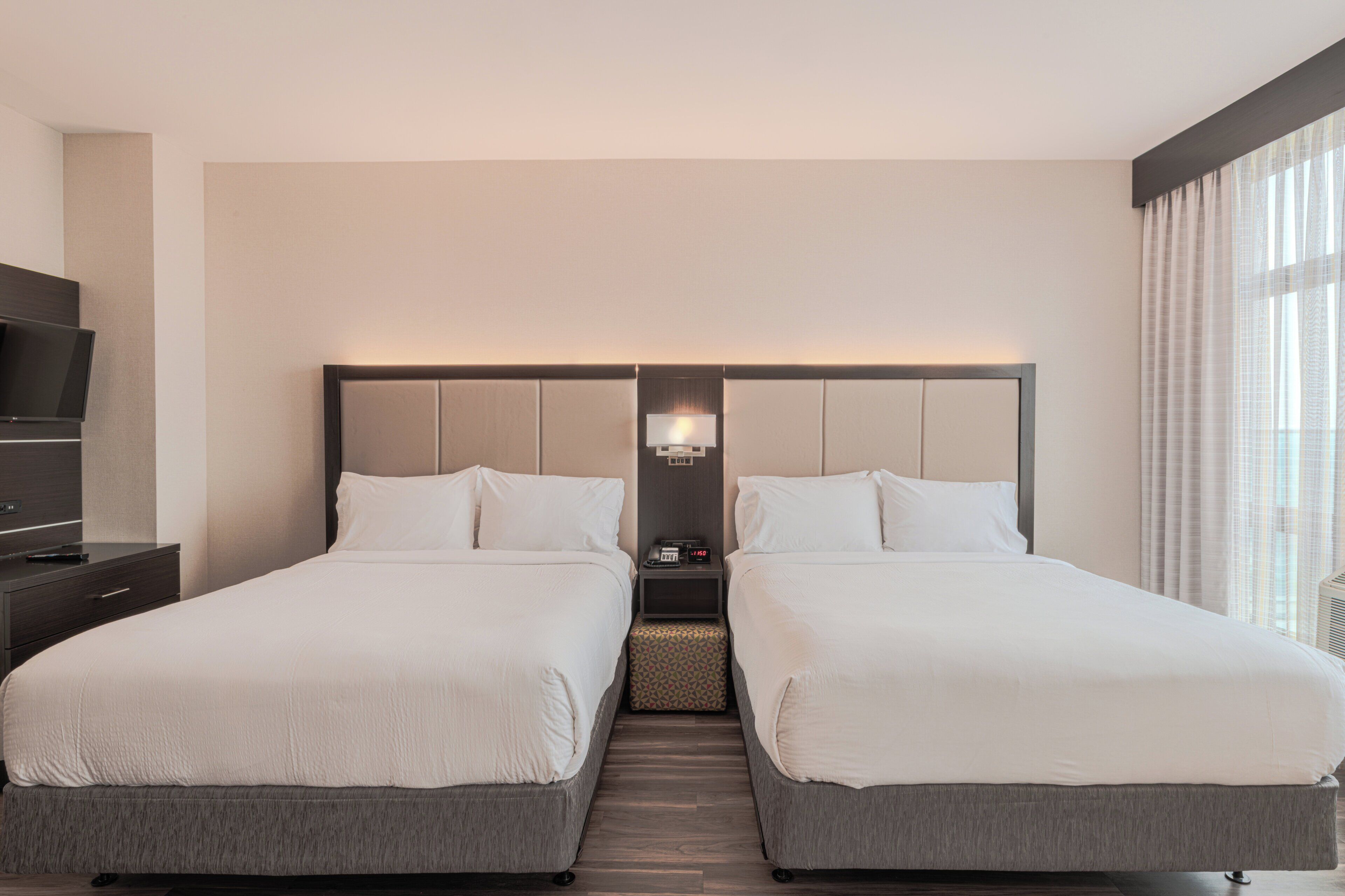 A hotel room with two beds, a TV, a nightstand, and a lamp.