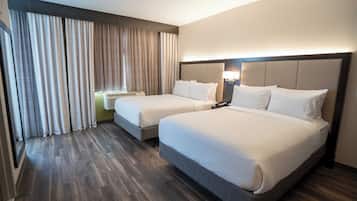 Habitación de hotel con dos camas, un ventanal con cortinas, un televisor de pantalla plana y una mesita de noche con lámpara.