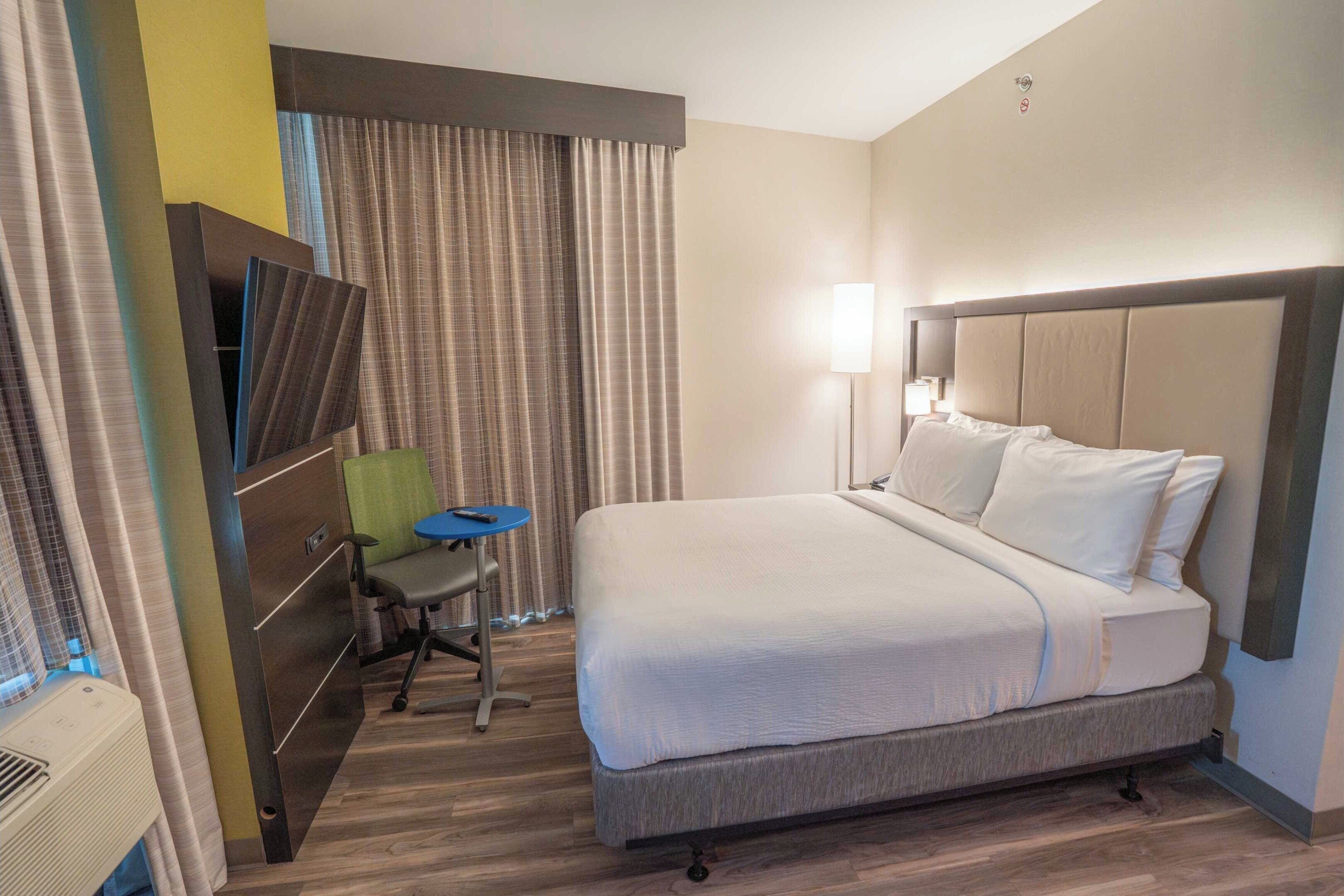 Une chambre d’hôtel avec un grand lit, un bureau avec une chaise, une lampe et des rideaux.
