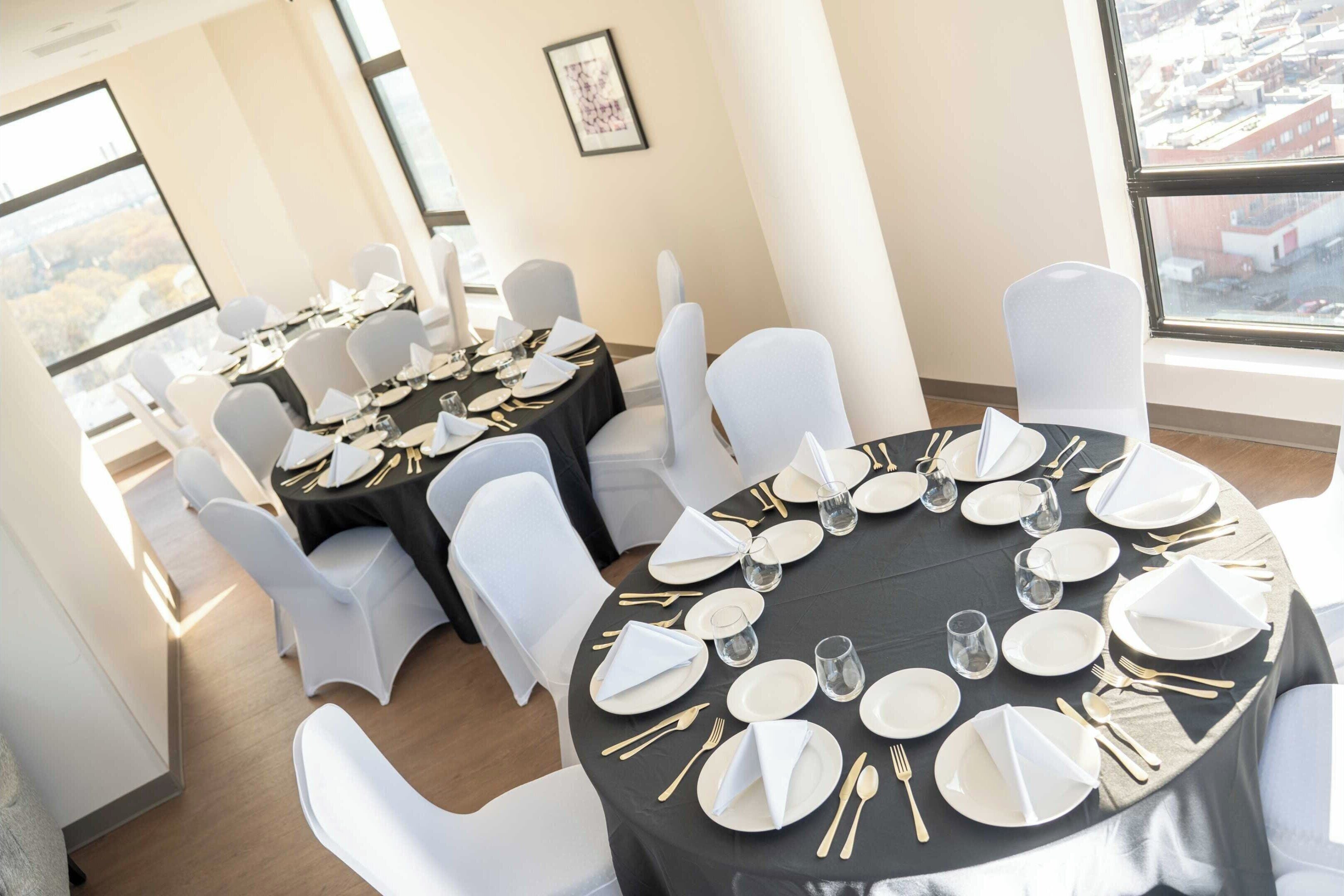 Une salle de conférence avec des tables rondes disposées pour une réunion, équipée de chaises blanches et de nappes noires.