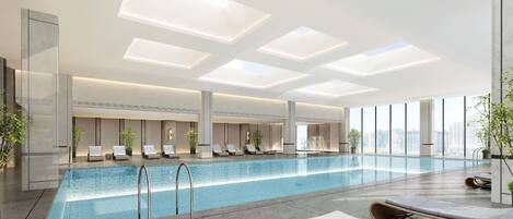 A modern indoor swimming pool with clear glass walls, lounge chairs, and potted plants.