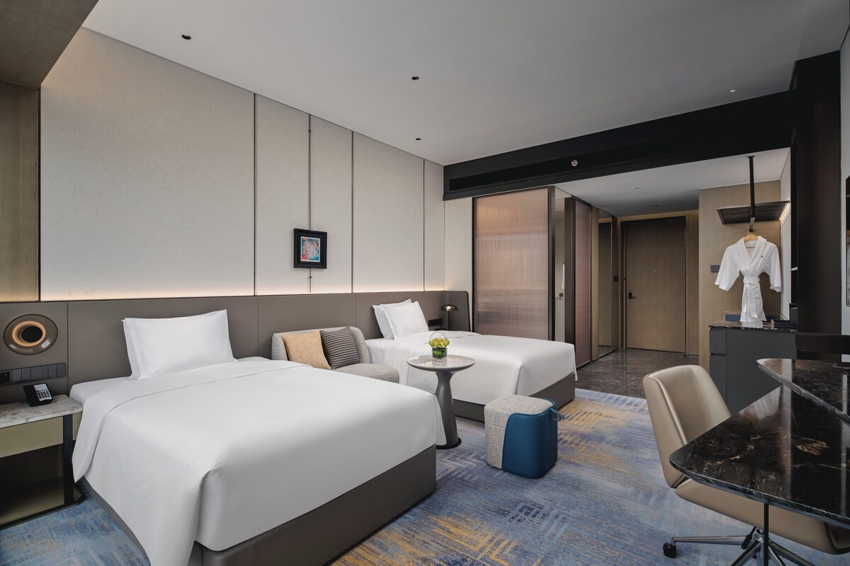 Una habitación de hotel moderna con dos camas, un escritorio, una mesita y un área de descanso.