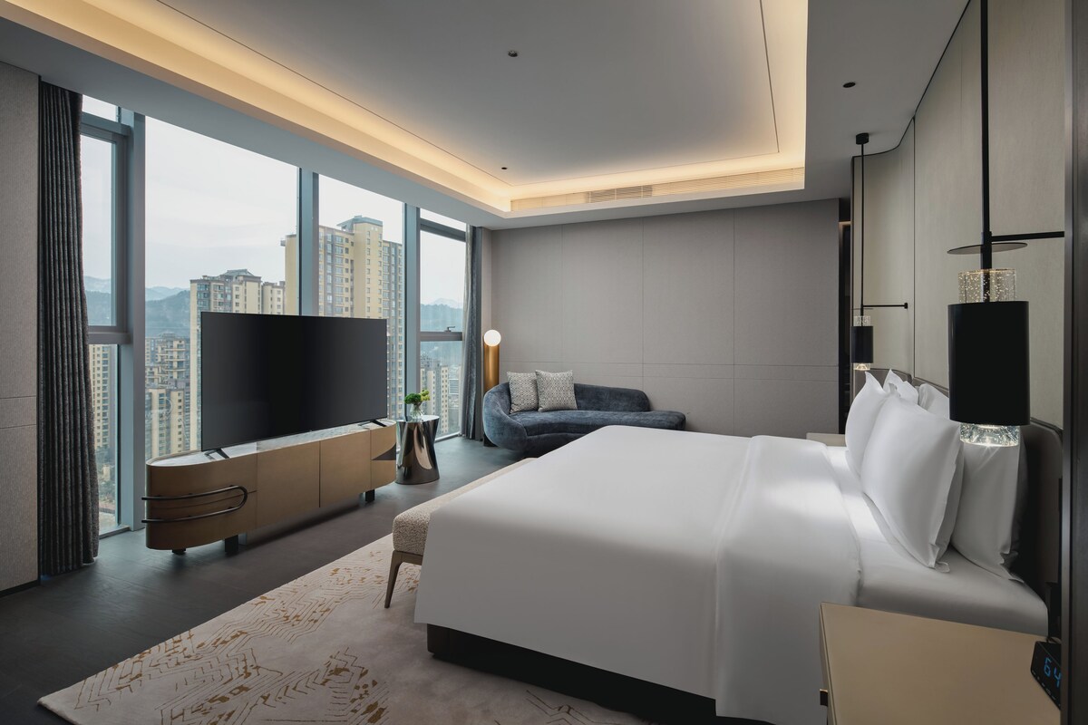 Un dormitorio moderno con una cama grande, un televisor y vistas a la ciudad.
