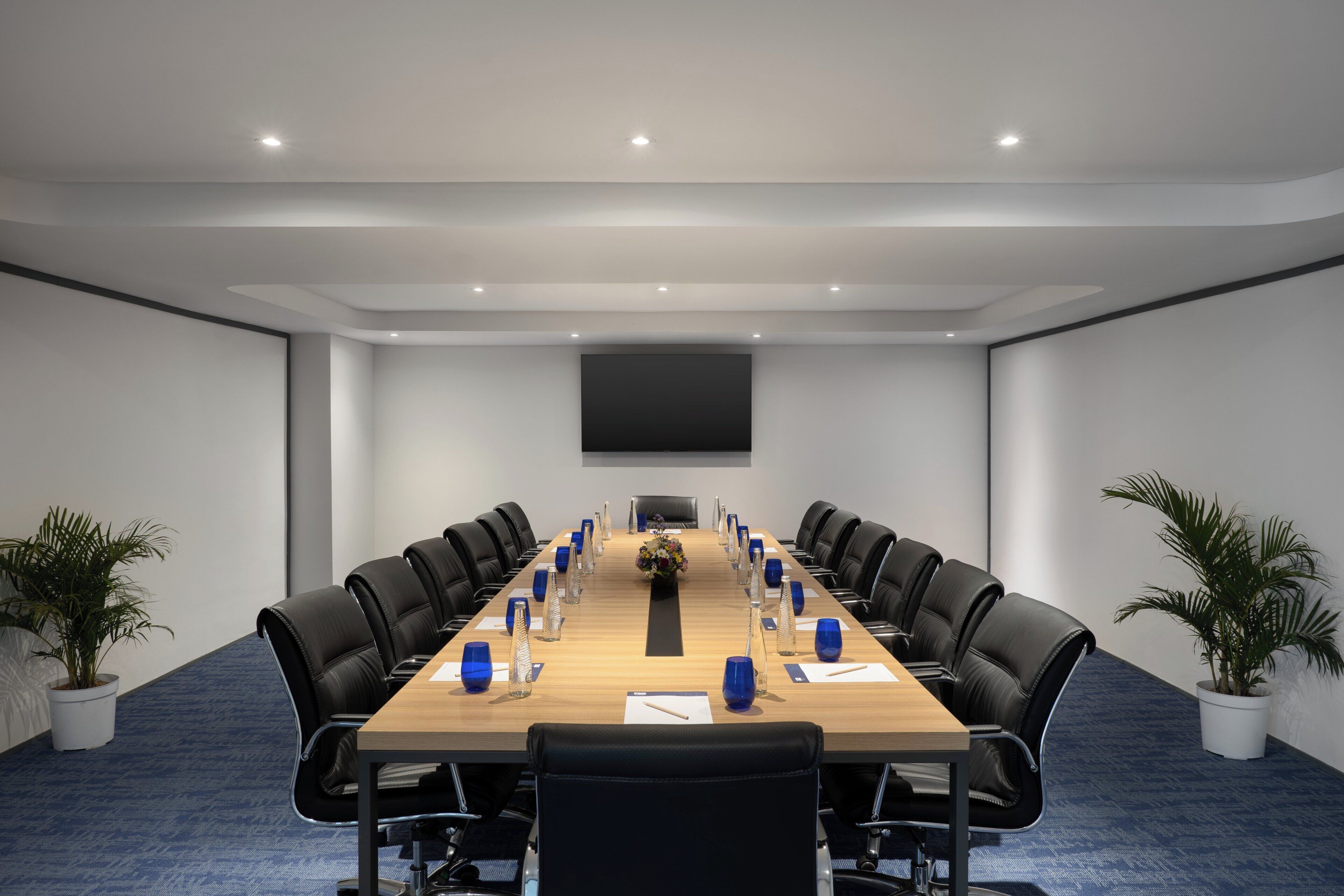 A conference room with a long table, black chairs, and potted plants.
