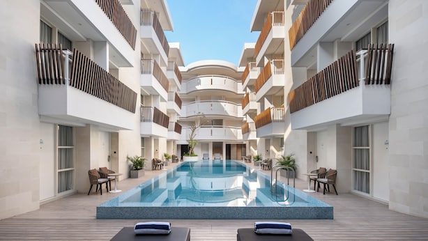 A modern hotel atrium with a central pool, multiple balconies, and outdoor seating areas.