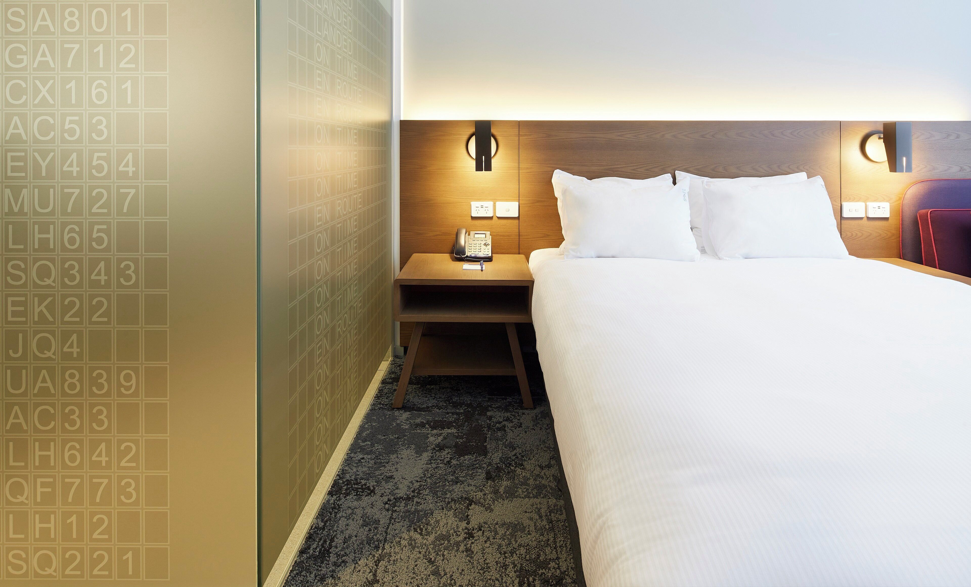 A hotel room with a bed, bedside tables, a telephone, and a wall with numbers.