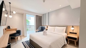 A modern hotel room with a large bed, a desk, a chair, and a balcony with curtains.
