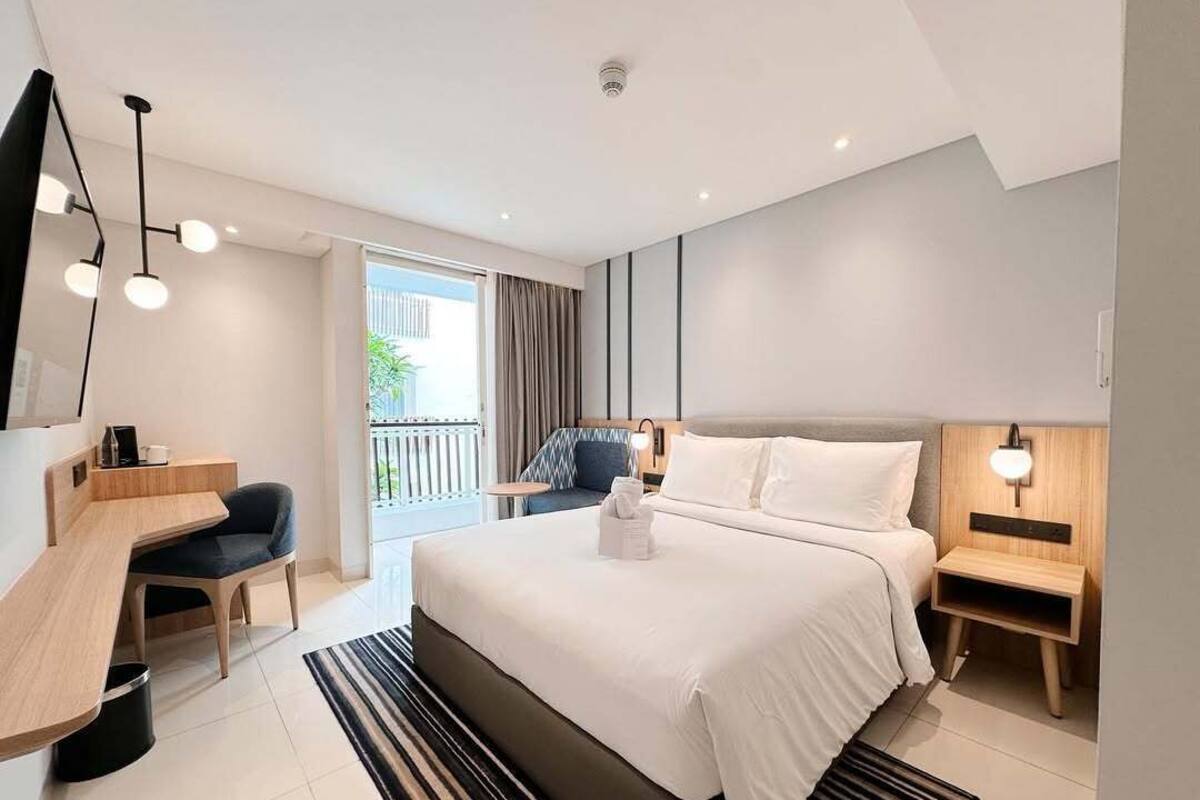 Une chambre d’hôtel moderne dotée d’un grand lit, d’un bureau, d’une chaise et d’un balcon avec des rideaux.