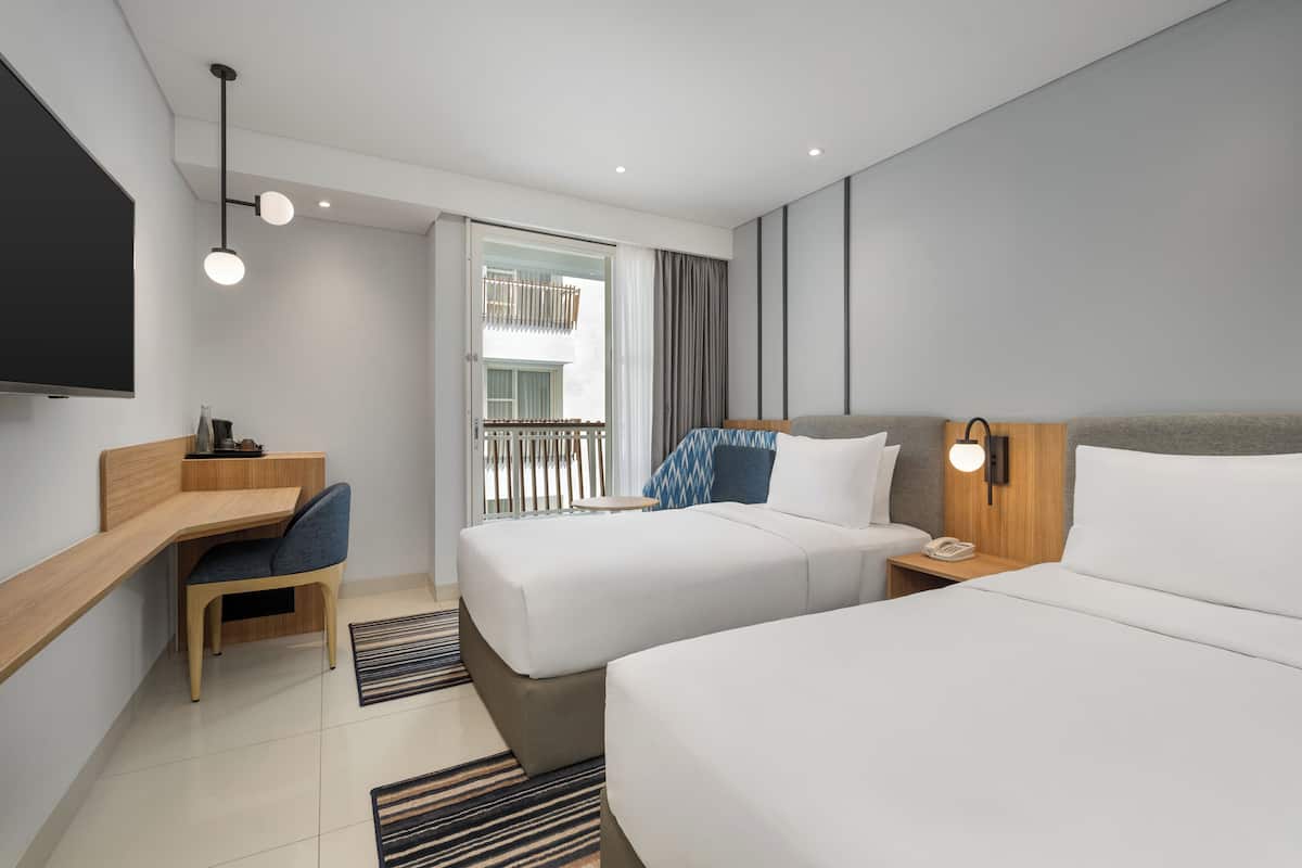 Une chambre d’hôtel moderne équipée de deux lits, d’un bureau, d’une chaise, d’une télévision et d’un balcon avec vue.