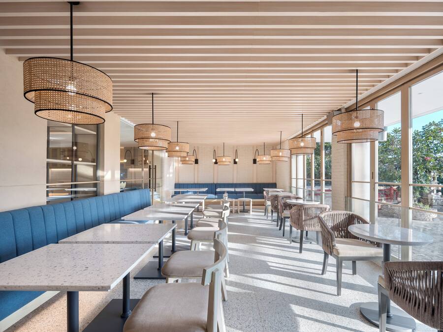 Un restaurante moderno con un amplio banco, mesas, sillas de mimbre y grandes ventanales con vistas.