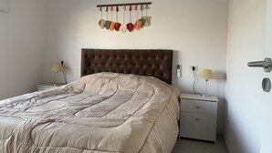 A bedroom with a tufted headboard, a beige quilted bedspread, two bedside tables with lamps, and a wall-mounted light fixture.