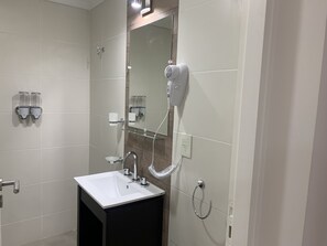 Un baño moderno con un lavamanos blanco, un espejo, un secador de pelo y dos dispensadores de jabón.