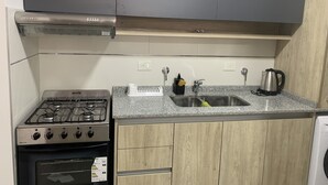 A kitchen with a gas stove, oven, stainless steel range hood, granite countertop, wooden cabinets, a sink with a faucet, and a kettle.