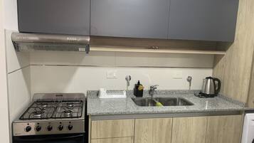 Cocina con estufa a gas, horno, campana extractora de acero inoxidable, encimera de granito, armarios de madera, pileta con grifo y tetera.