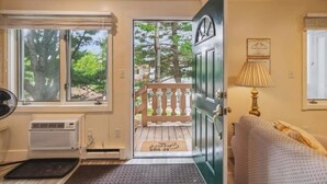 Une pièce avec une grande fenêtre, une porte donnant sur l’extérieur, un radiateur, un banc à l’extérieur et une lampe sur la droite.