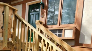 Un escalier en bois mène à une maison avec une porte verte et une fenêtre équipée de stores.