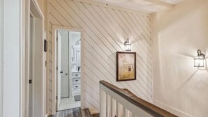 Un escalier en bois avec une rampe blanche mène à une pièce dotée d’une porte blanche et d’un tableau encadré accroché au mur.