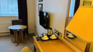 Une chambre d’hôtel avec un bureau en bois, une chaise, une télévision, un miroir et une fenêtre avec des rideaux.