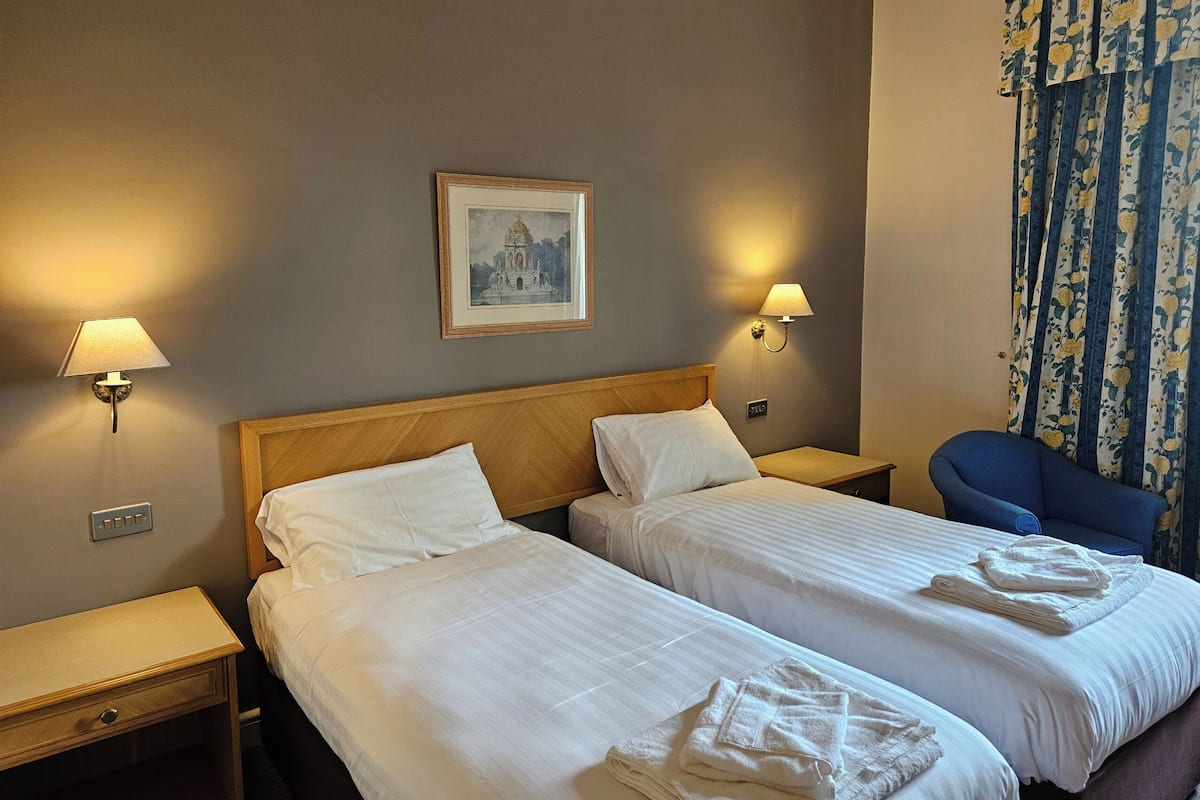 Une chambre d’hôtel avec deux lits, une table de chevet, une lampe, un tableau accroché au mur et une chaise.
