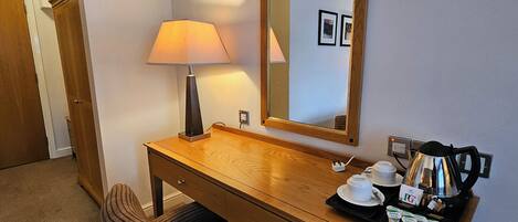 A hotel room with a wooden desk, a chair, a lamp, a mirror, and a tray with toiletries.