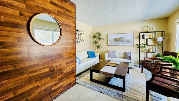 A modern living room with a wooden accent wall, a round mirror, a white sofa, a coffee table, and a bookshelf.