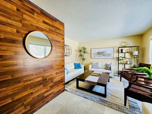 Una sala de estar moderna con una pared de acento de madera, un espejo redondo, un sofá blanco, una mesa de centro y una estantería.