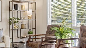 A living room with a dark wooden chair, a metal bookshelf, and a large window with blinds.