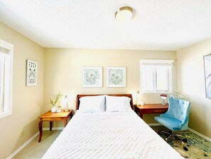 A bedroom with a large bed, two bedside tables, a chair, and artwork on the walls.