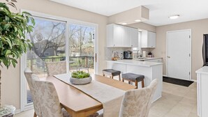 A modern kitchen with white cabinets, a central island, and a dining area with a table and chairs.
