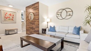 A living room with a wooden accent wall, a white sofa with blue cushions, a coffee table, a lamp, and a framed picture on the wall.