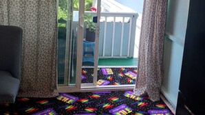 Quarto com porta de correr de vidro que dá para uma varanda. O quarto possui piso estampado e uma televisão à direita.
