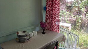 Uma área de refeições com uma mesa posta para dois, um vaso com flores e vista para o verde lá fora.