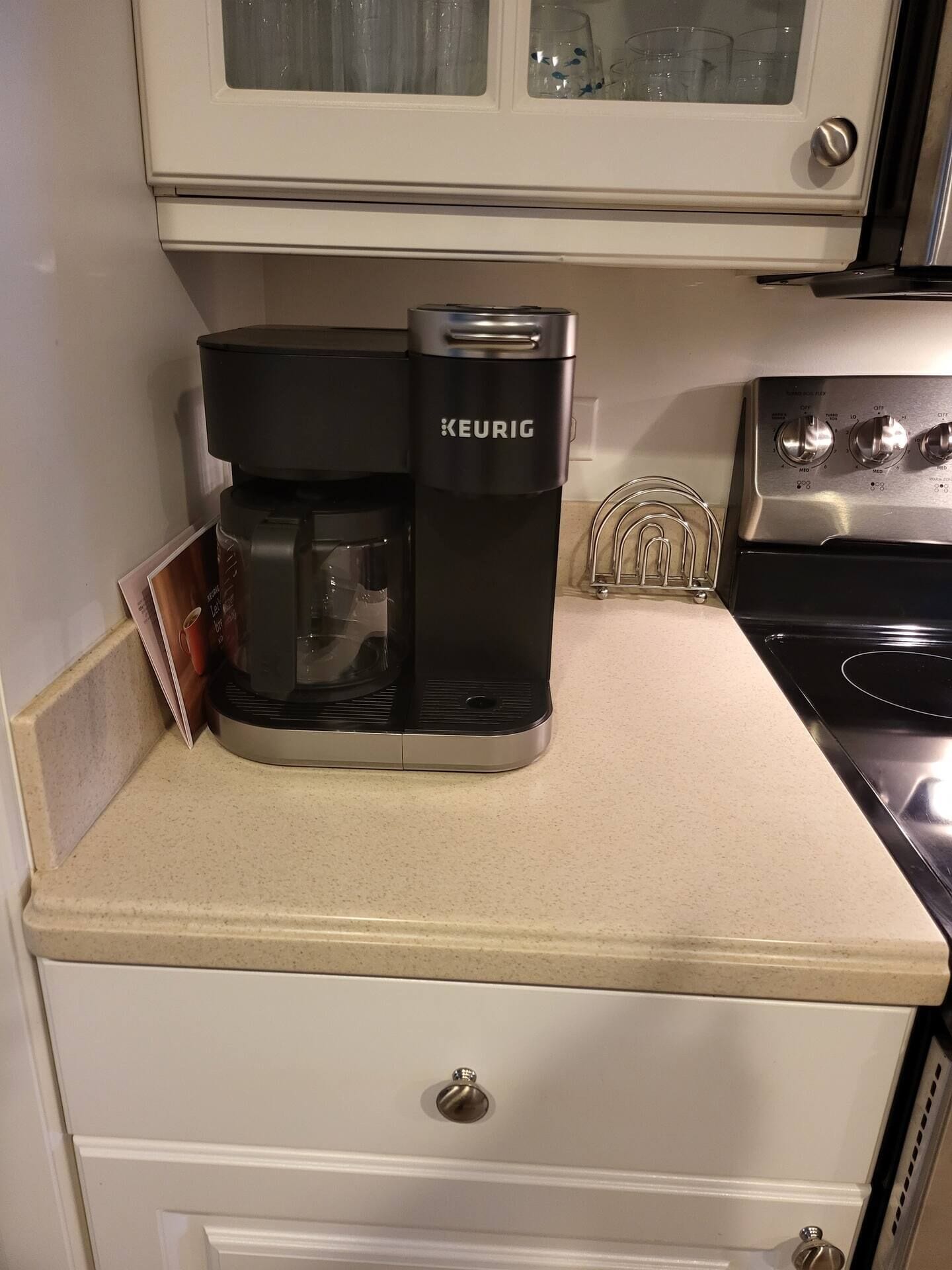Una cafetera Keurig sobre una encimera de cocina, con un armario encima.