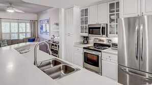 A modern kitchen with stainless steel appliances, white cabinetry, and a large island with a sink. - Coligny Beach, Pools, & Shops- Few Steps Away (Hilton Head Island)