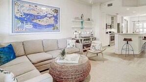 A modern living room with a beige sofa, a round wicker ottoman, and a large map on the wall. - Coligny Beach, Pools, & Shops- Few Steps Away (Hilton Head Island)