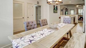 A dining area with a long table, cushioned chairs, and a chandelier. - Coligny Beach, Pools, & Shops- Few Steps Away (Hilton Head Island)