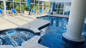 Piscina interior con azulejos azules, rodeada de columnas blancas y sillas azules.