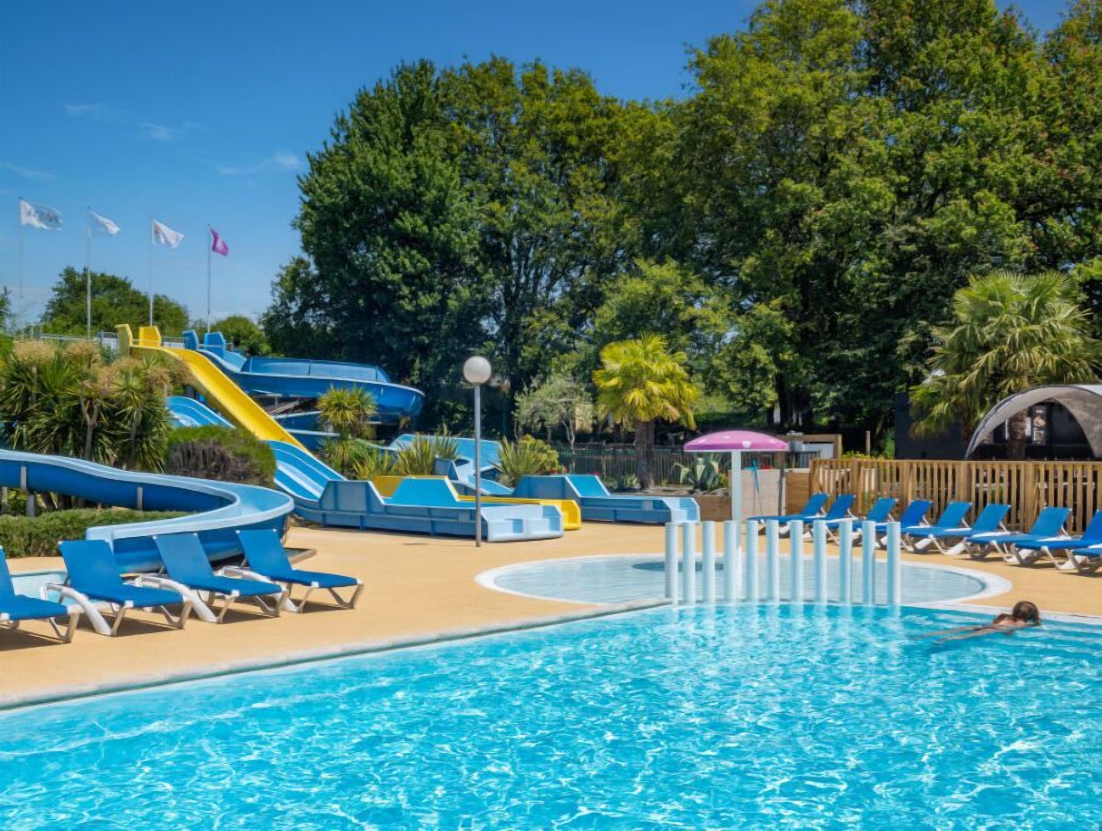 A swimming pool with a water slide, lounge chairs, and a covered seating area.