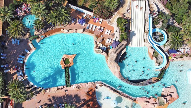 Eine Vogelperspektive eines Resorts mit mehreren Schwimmbecken, Liegestühlen und Palmen.