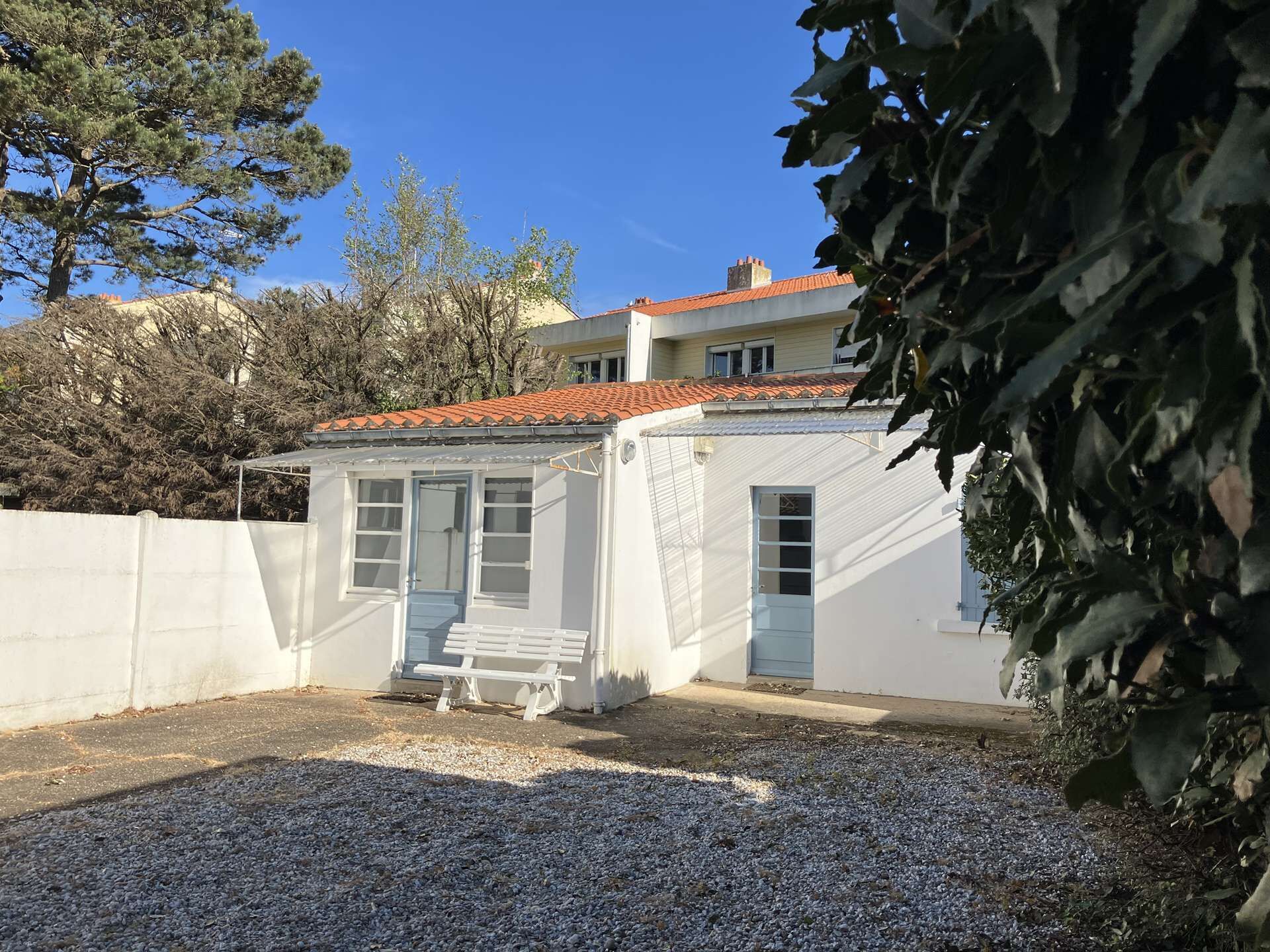 A white building with a red-tiled roof, a bench, and a gravel driveway.