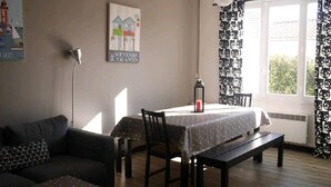 A living room with a sofa, a dining table with chairs, a lamp, and a poster on the wall.