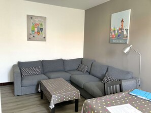 En stue med en grå sofa, et lille bord med et prikket dug og to puder med et sort og hvidt mønster.