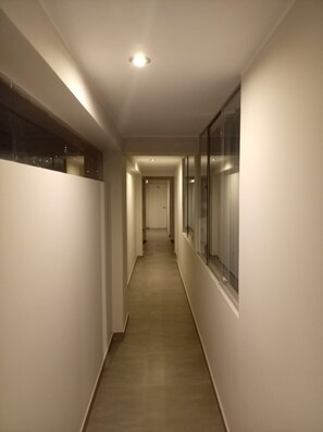 Un pasillo estrecho y bien iluminado con piso de madera, que conduce a una puerta al final.